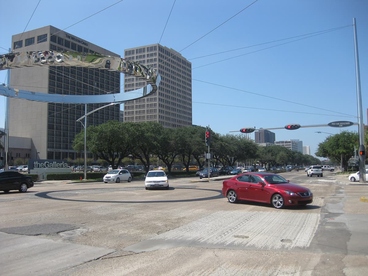 The intersection of Westheimer Road and Post Oak Boulevard in Houston, with traffic signals, passing cars and The Galleria and a Westin hotel across the street